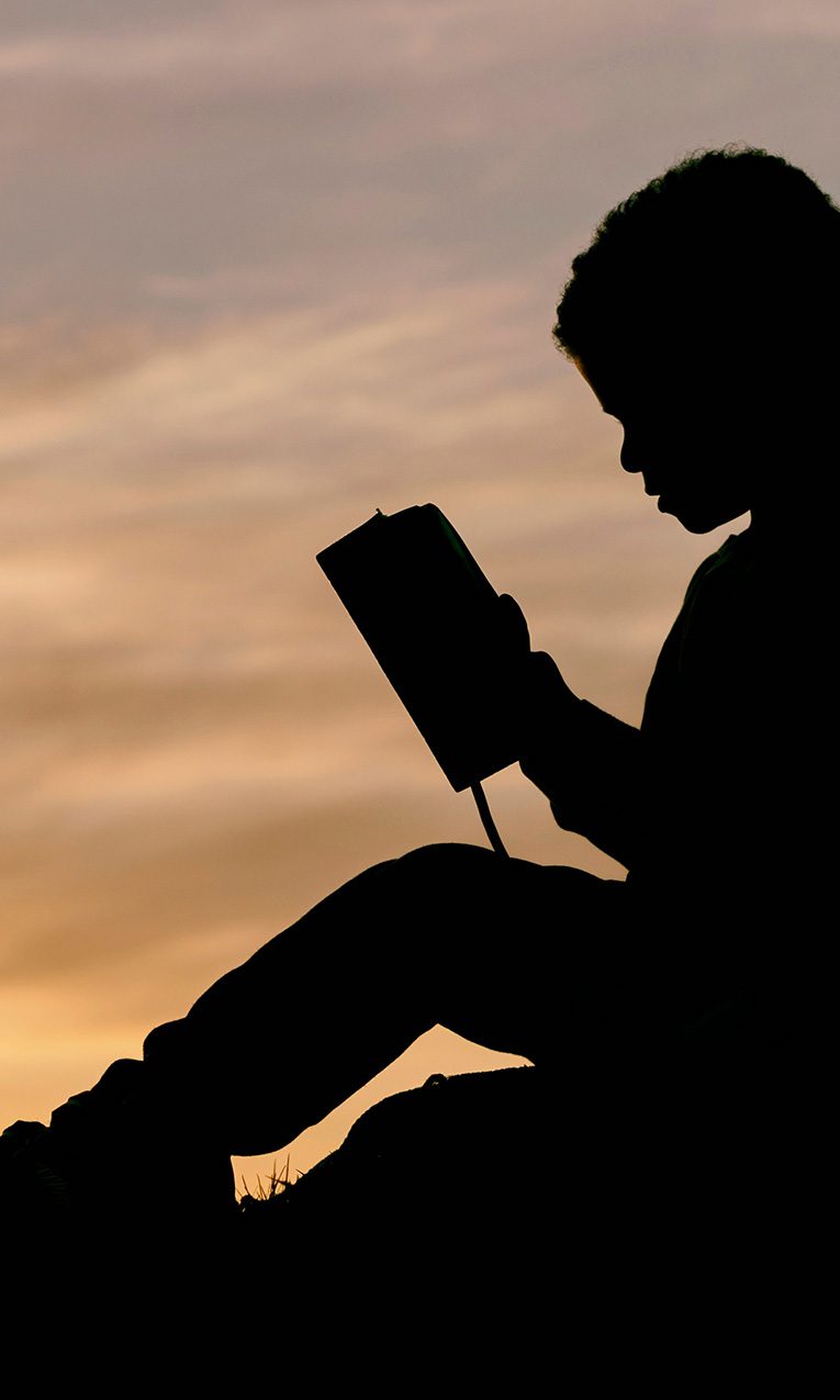silhouette of a boy reading the Bible