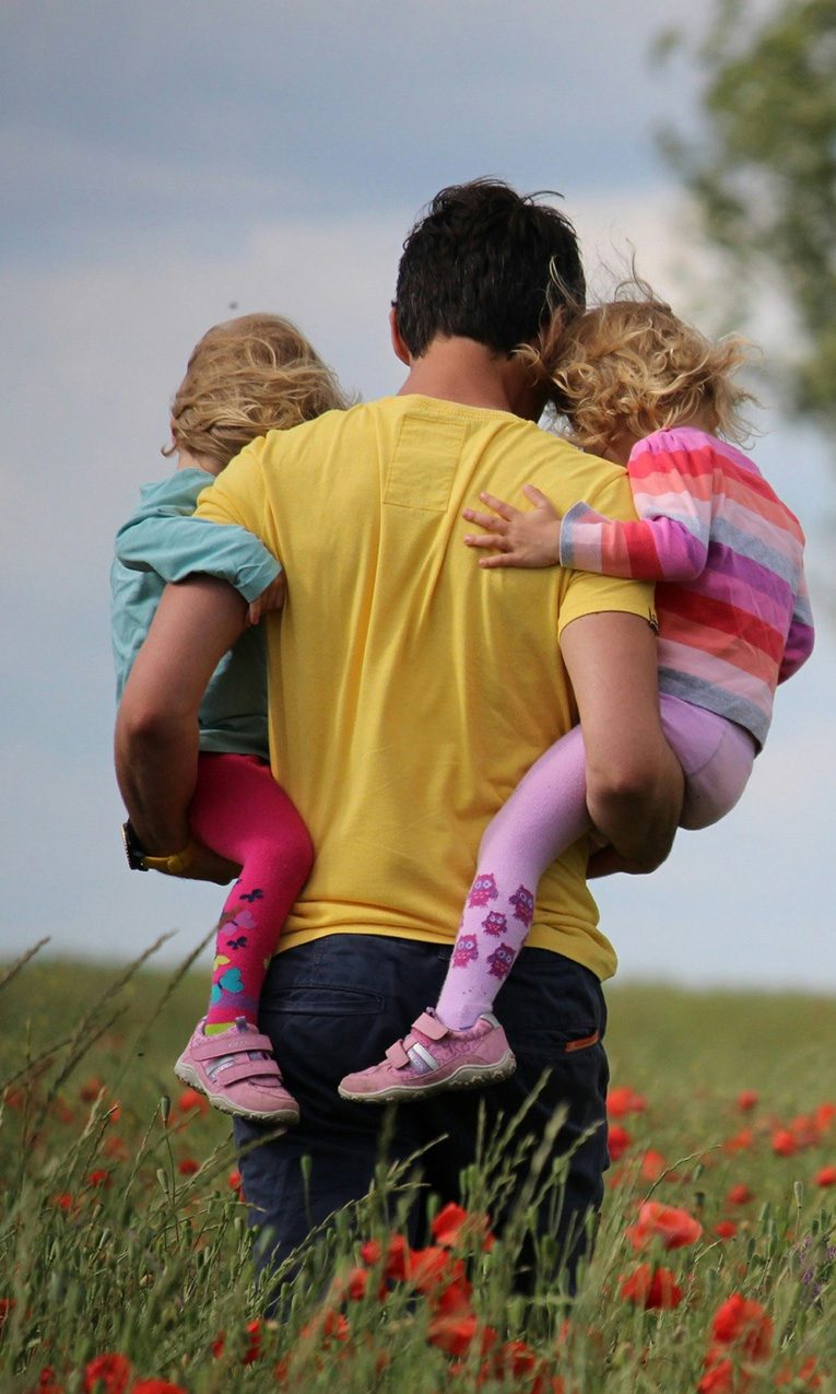 a man carrying two girls while walking on a field