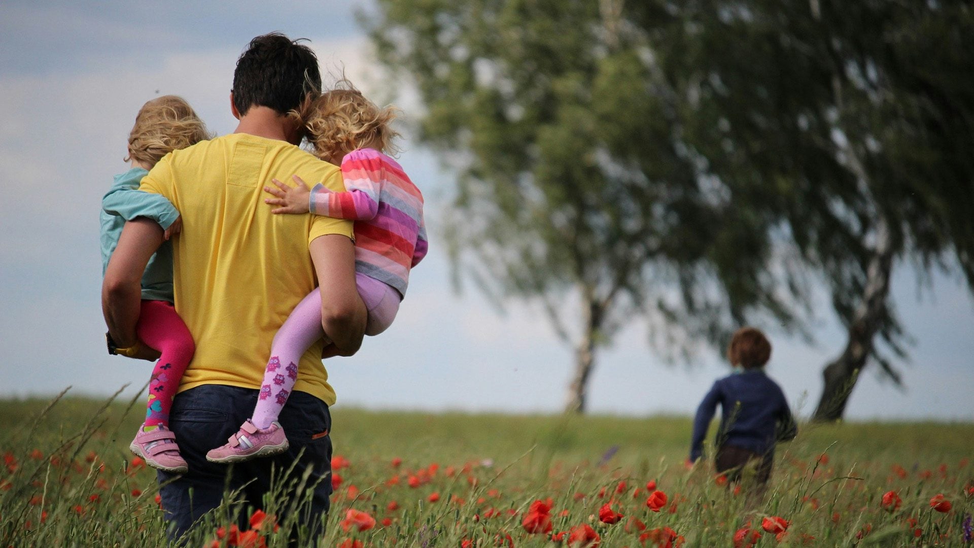 a man carrying two girls while walking on a field
