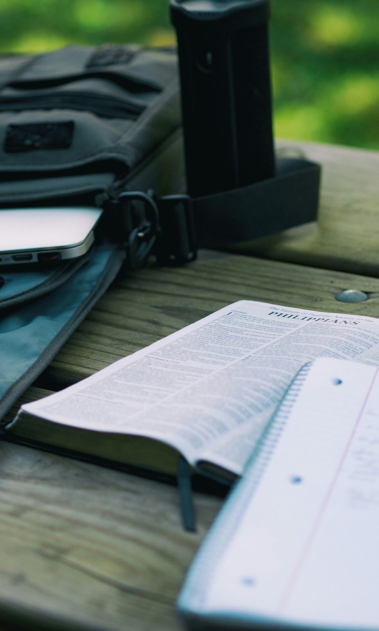 a laptop on a backpack next to a Bible, a notebook, and a pencil