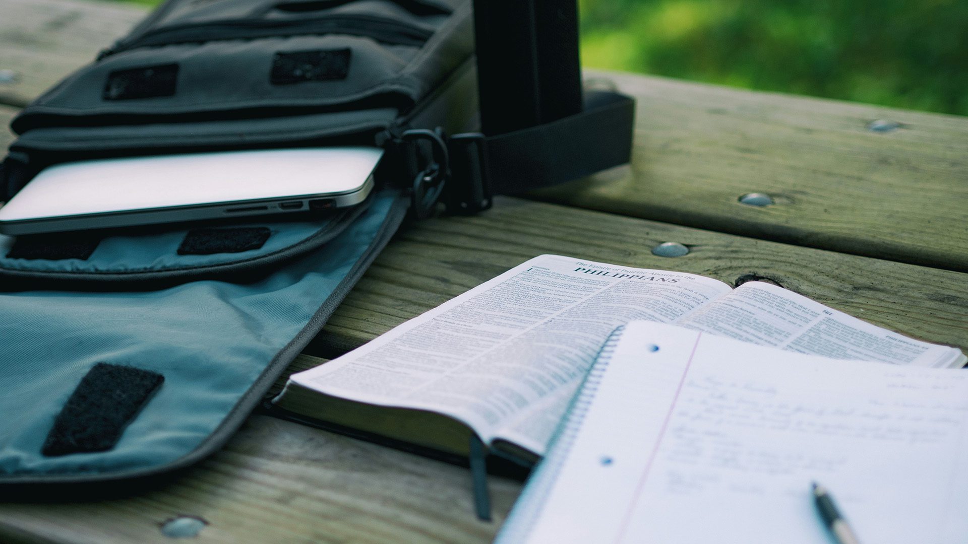 a laptop on a backpack next to a Bible, a notebook, and a pencil