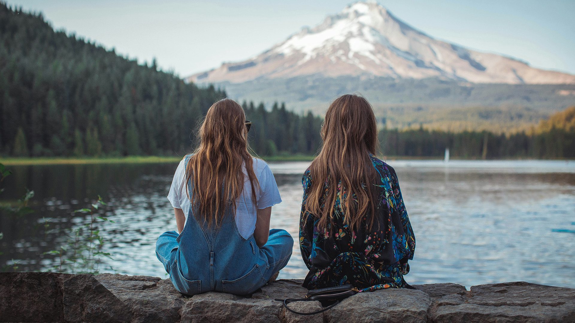 two women sitting on rock wall near body of water