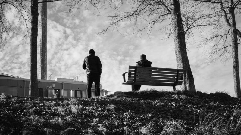 Two men having a conversation by a bench.