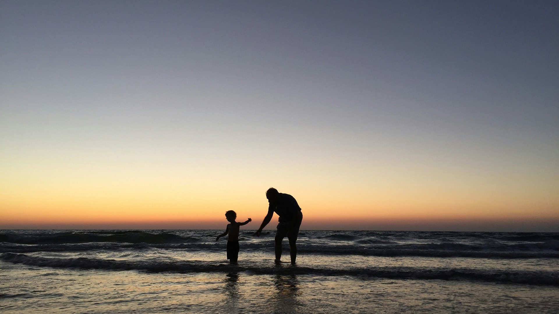 Silhouette of a man playing with his son at the beach.