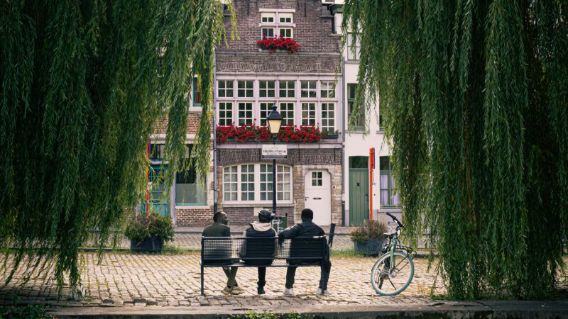 Three men having a conversation on a bench in front of a house.