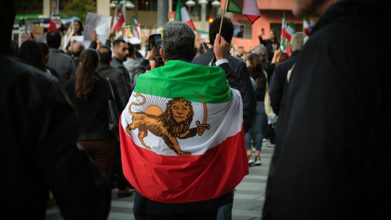 A man wearing an Iranian flag at a protest.