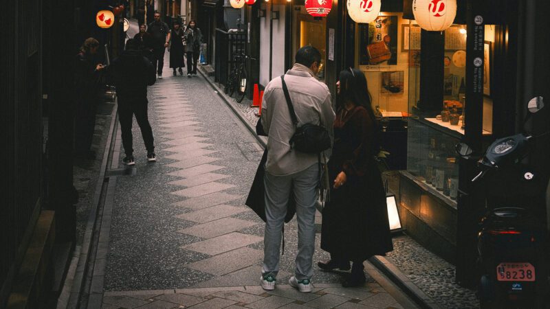 People walking down a narrow street with lanterns.