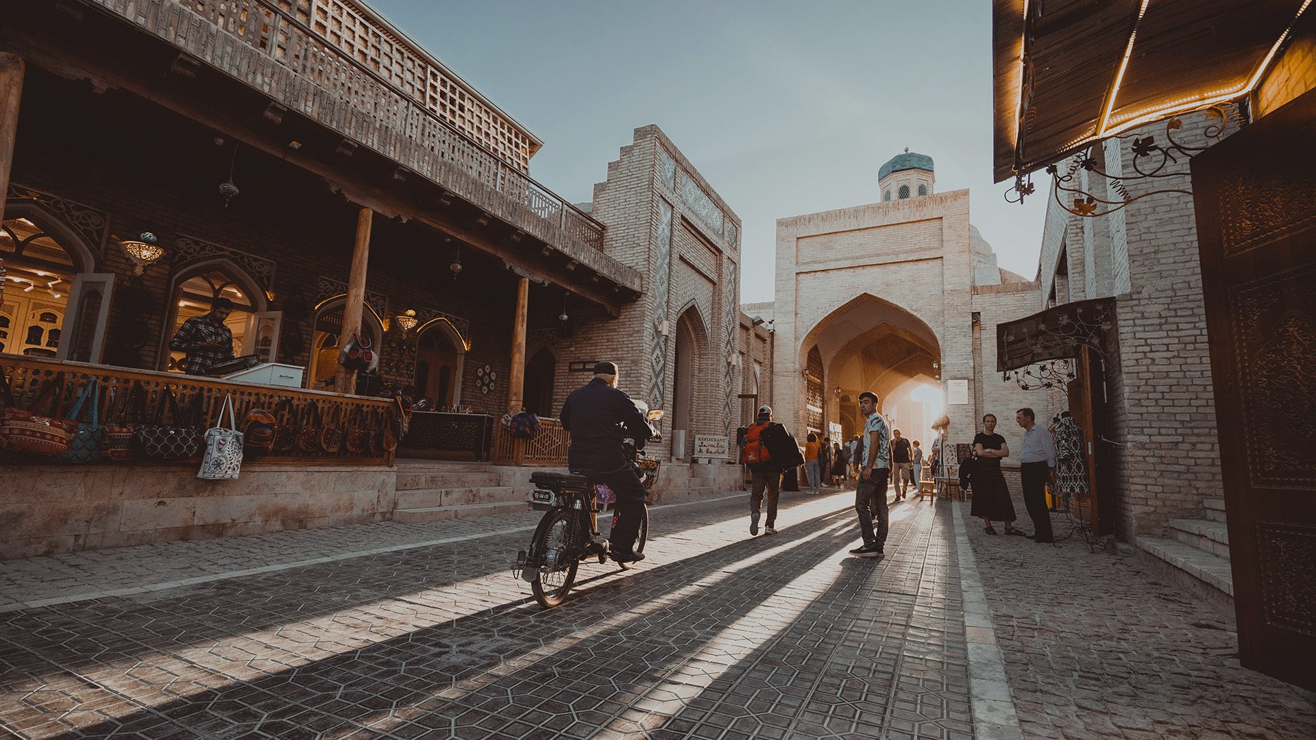 A person riding a bicycle on a brick road between buildings.