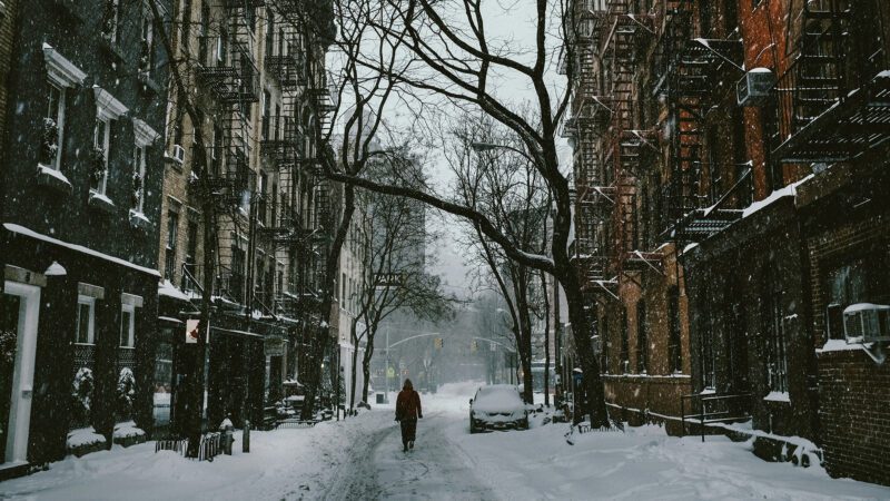 A man walking through a street filled with snow.