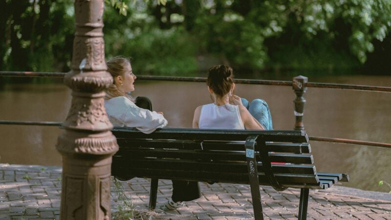 Two girls talking on a bench.